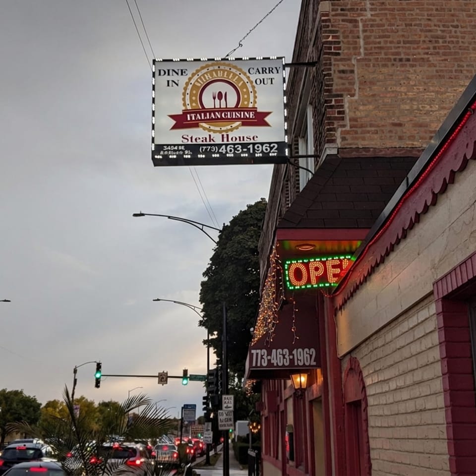 Street view of an Italian steakhouse with a lit open sign, hanging restaurant sign, and traffic at dusk.